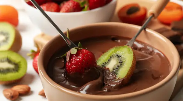 Fragole e kiwi immersi in una fonduta di cioccolato, un delizioso esempio di abbinamenti cioccolato e frutta.