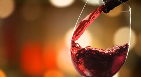 Versare vino rosso in un bicchiere, un momento allappante significato di piacere e convivialità, con luci sfocate sullo sfondo.
