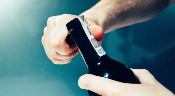 Mani che aprono una bottiglia di vino, rimuovendo la capsula.