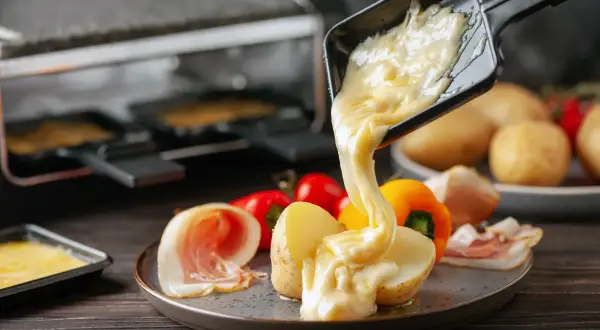 Formaggio fuso che cola su patate e salumi, un delizioso esempio di diversi tipi di formaggio usati per la raclette.
