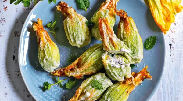 Fiori di zucca fritti, ripieni di formaggio cremoso e guarniti con menta fresca, su un piatto blu.