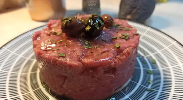 Un delizioso tartare di carne cruda, guarnito con olive nere e erba cipollina, pronto per essere gustato.