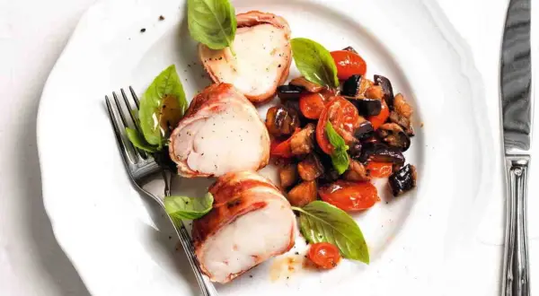 Tranci di rana pescatrice avvolti nel prosciutto, serviti con ratatouille di verdure e basilico fresco.