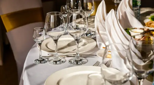Tavola apparecchiata con bicchieri vuoti e tovaglioli piegati. Il galateo bottiglia di vino finita è rispettato, si attende il prossimo servizio.