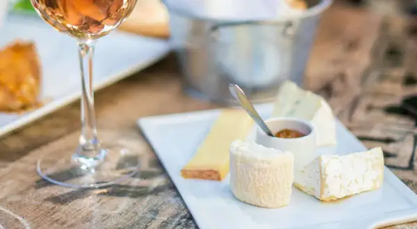 Calice di vino rosato accanto a un tagliere di formaggi, con un assaggio di passito di Pantelleria.