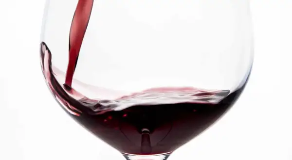 Vino rosso porpora versato in un calice, creando un vortice invitante.