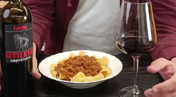 Un bicchiere di vino rosso e un piatto di pasta al ragù, accompagnati da una bottiglia di Gutturnio.