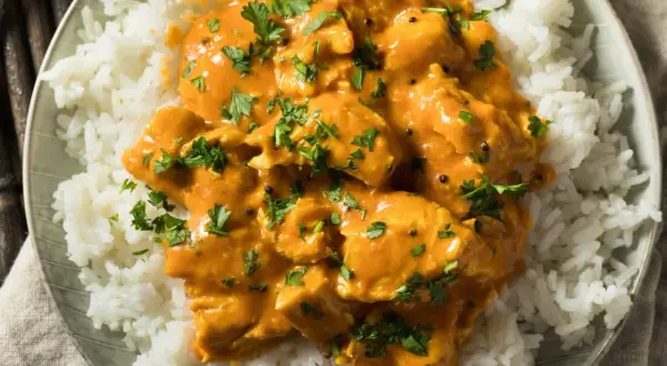 Piatto di riso bianco con pollo al curry arancione, guarnito con prezzemolo fresco. Perfetto con vino bianco o rosso.