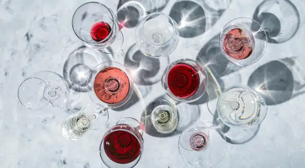Vari calici di vino rosso, rosato e bianco, con ombre suggestive. La temperatura ideale per gustare un buon vino rosso è fondamentale.