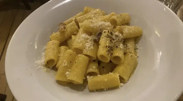 Piatto di rigatoni alla carbonara, conditi con guanciale croccante, pecorino romano e pepe nero. Perfetto con un bicchiere di vino bianco secco.