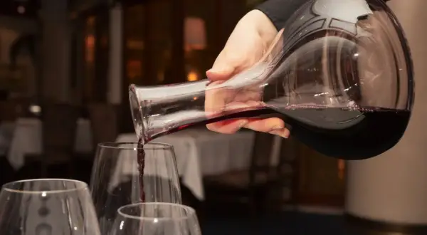 Mano versa vino rosso da una caraffa in bicchieri trasparenti, creando un'atmosfera elegante.