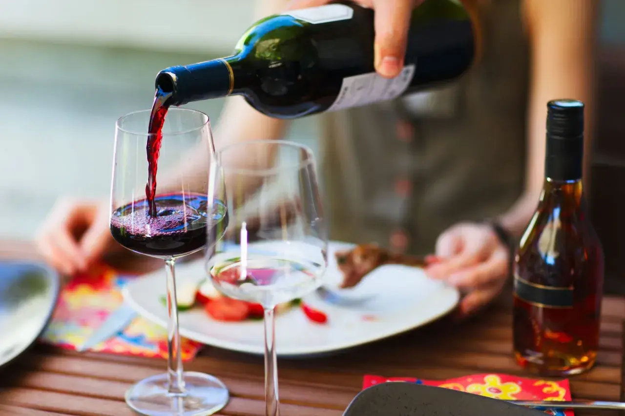 Versando vino rosso in un bicchiere, pronto per un perfetto abbinamento cibo vino con un piatto di carne e verdure.