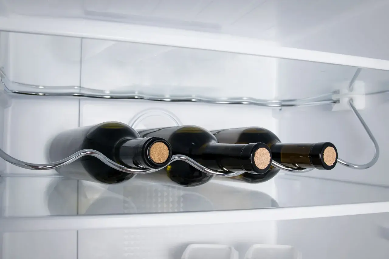 Bottiglie di vino bianco su un ripiano cromato all'interno di un frigorifero.