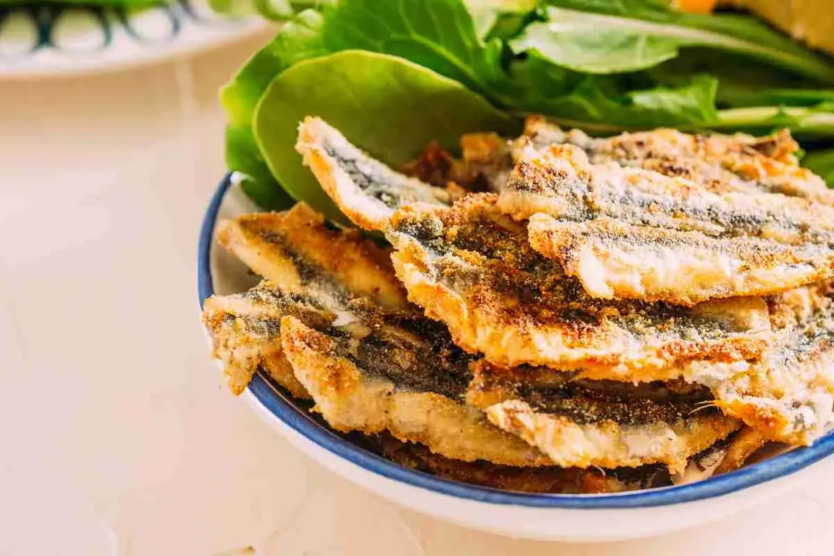 Piatto di alici fritte dorate e croccanti, servite con foglie verdi fresche.