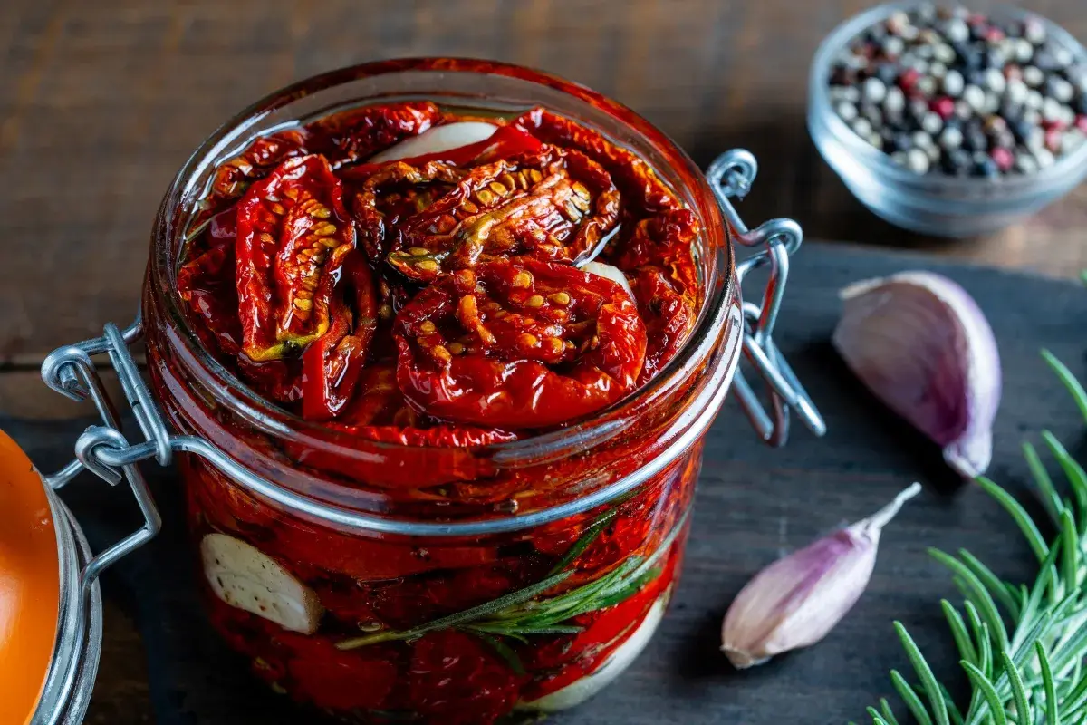 Pomodori secchi sott'olio in un barattolo, con aglio e rosmarino. Un sapore intenso che evoca l'umami, significato di gusto profondo.