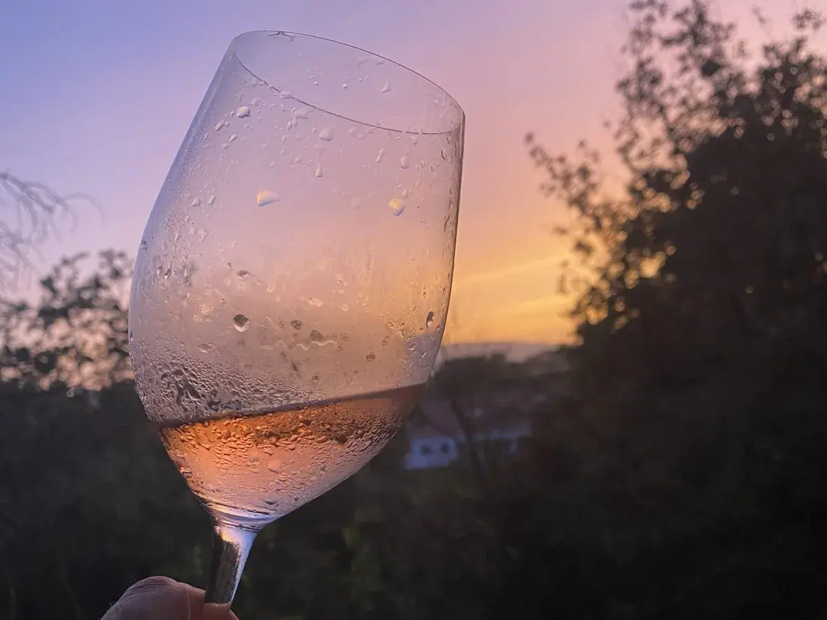 Calice di vino rosato, con gocce di condensa, al tramonto. Un brindisi alla vinificazione in rosato.
