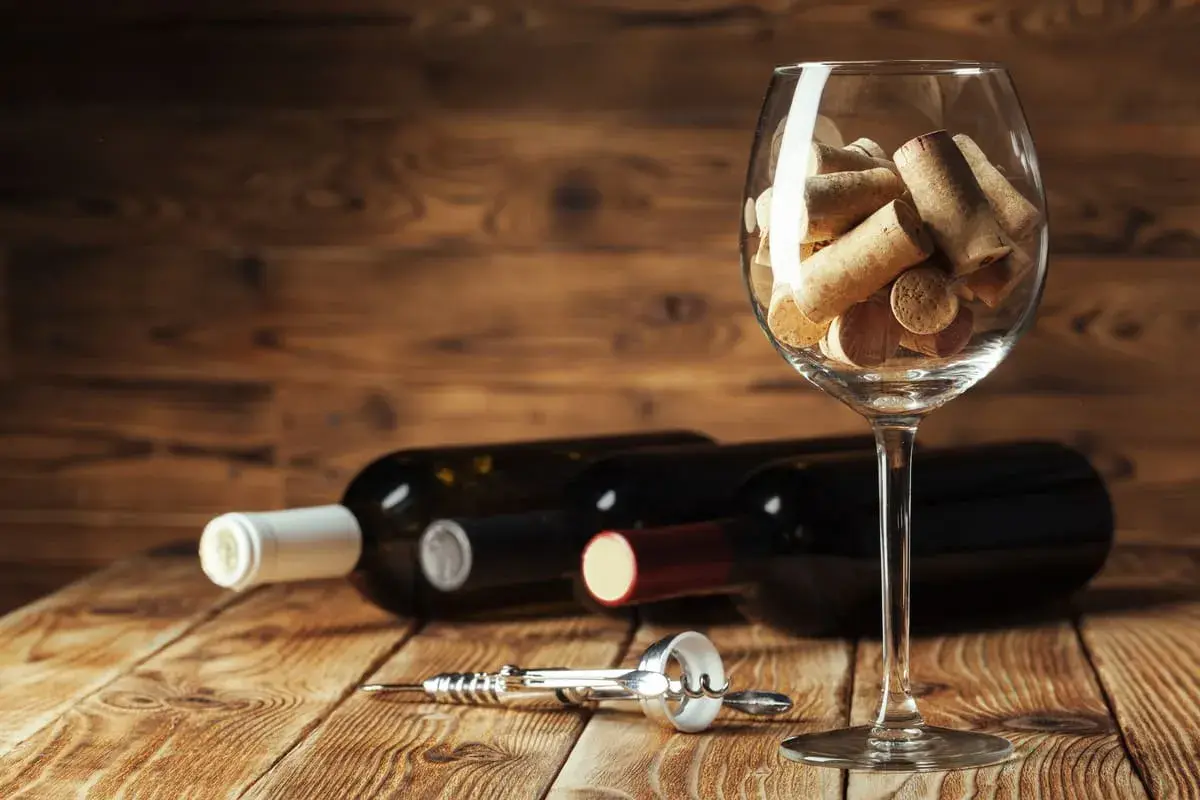 Calici pieni di tappi, bottiglie e cavatappi su un tavolo di legno. Un promemoria visivo dell'ossidazione del vino e del tempo che passa.