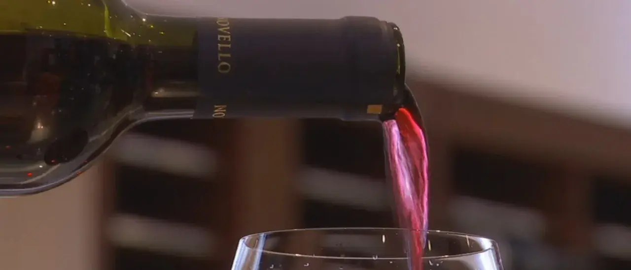 Versando vino rosso da una bottiglia con tappo a vite. Il liquido scorre nel bicchiere, creando un'onda cremisi.