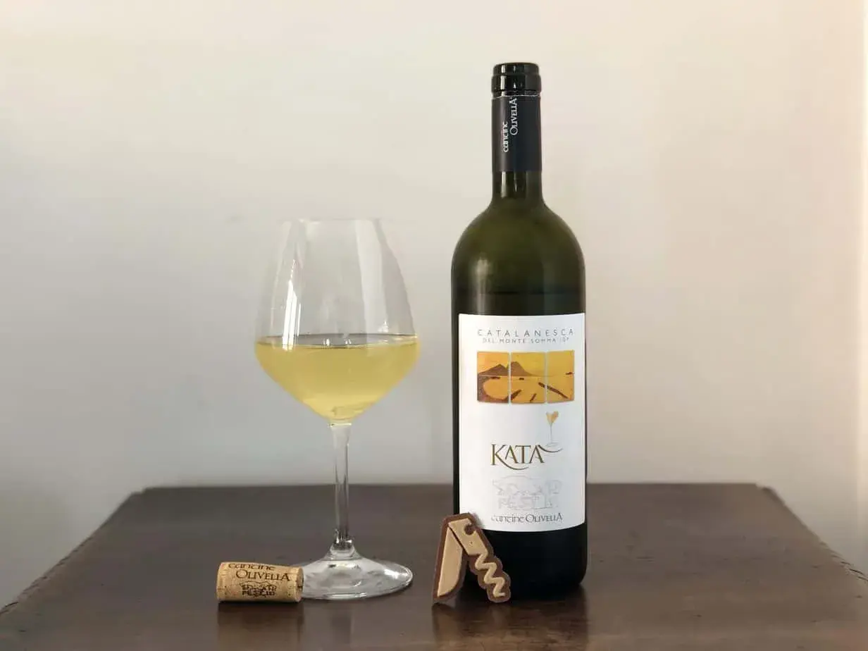 Un bicchiere di vino bianco e una bottiglia di Catalanesca del Vesuvio, con tappo e cavatappi sul tavolo.