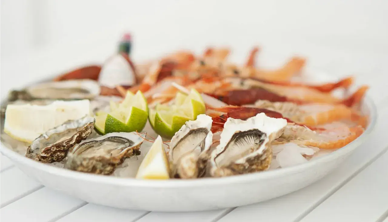 Piatto di ostriche fresche e gamberi, guarnito con spicchi di limone e lime. Un delizioso pesce bianco pronto da gustare.