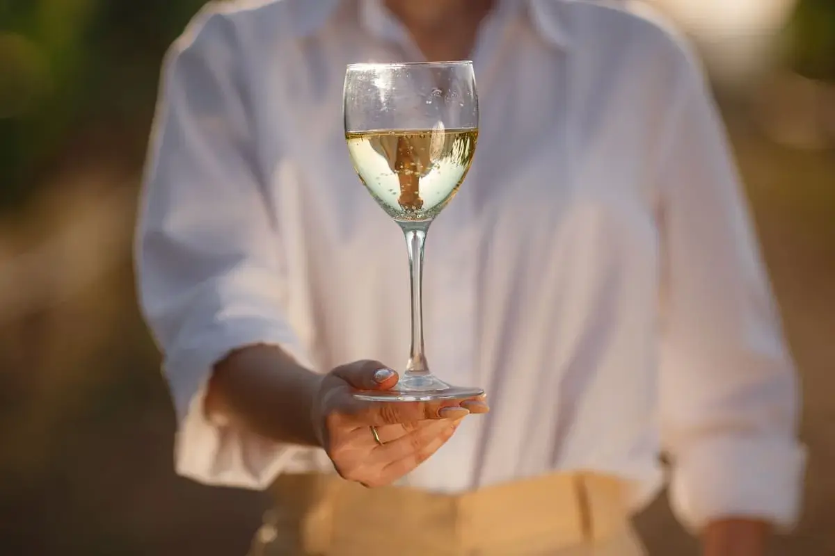 Un bicchiere di vino bianco, limpido e dorato, riflette la luce. Un invito a scoprire come si fa il vino bianco, un processo che trasforma l'uva in questa bevanda.