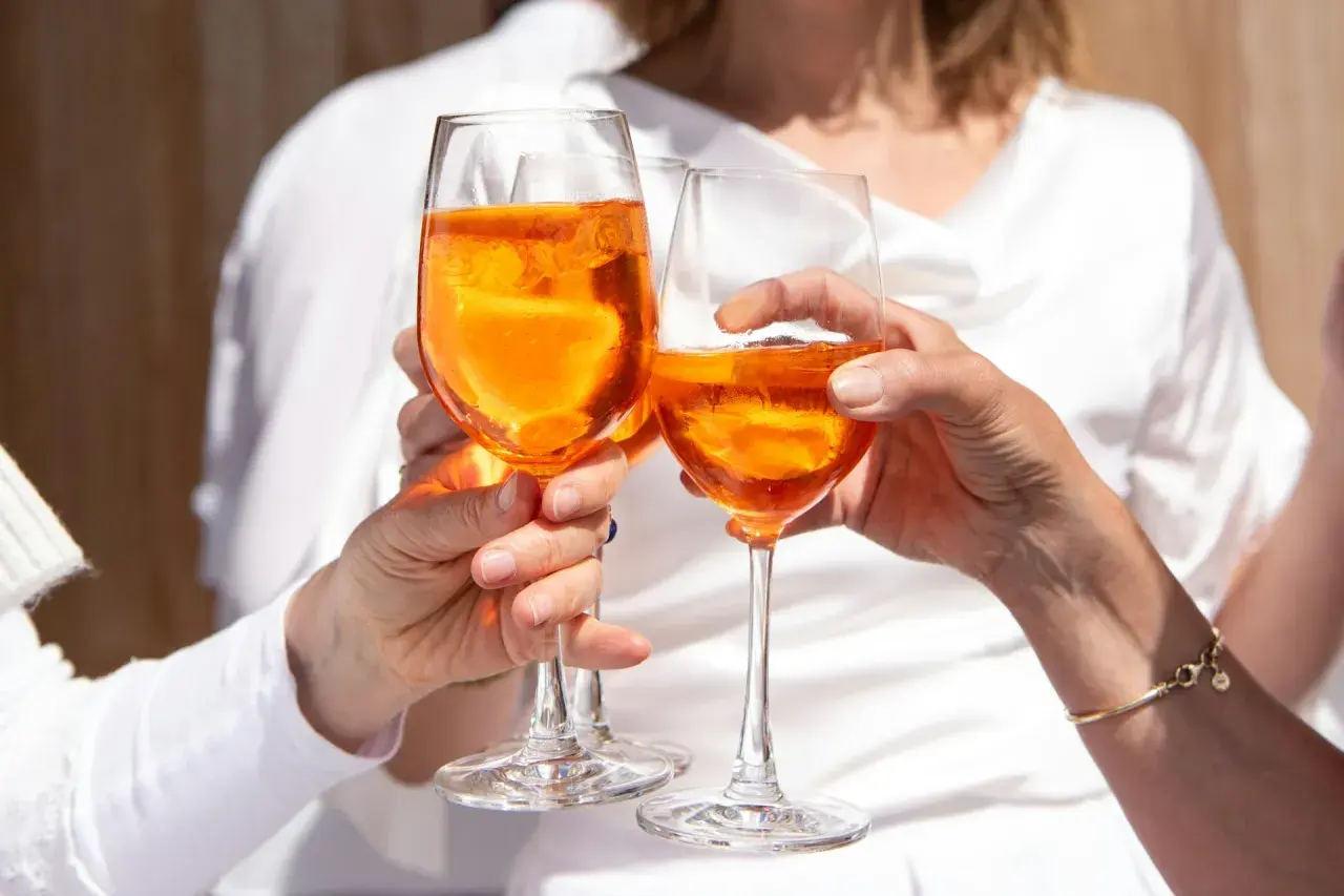 Tre mani brindano con bicchieri di Spritz arancione, un momento di gioia e leggerezza, pensando alle calorie spritz.