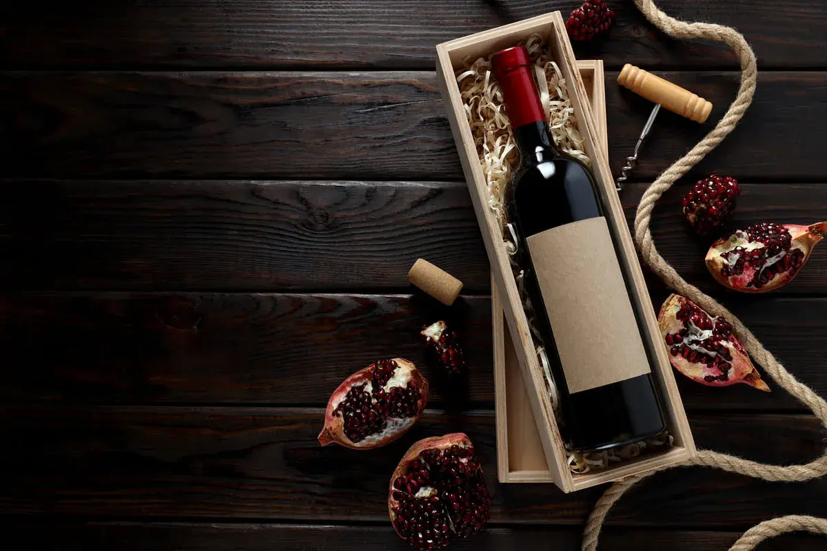 Una bottiglia di vino rosso in una scatola di legno, circondata da melograni e corda. Un assaggio dei **vini campani** più pregiati.