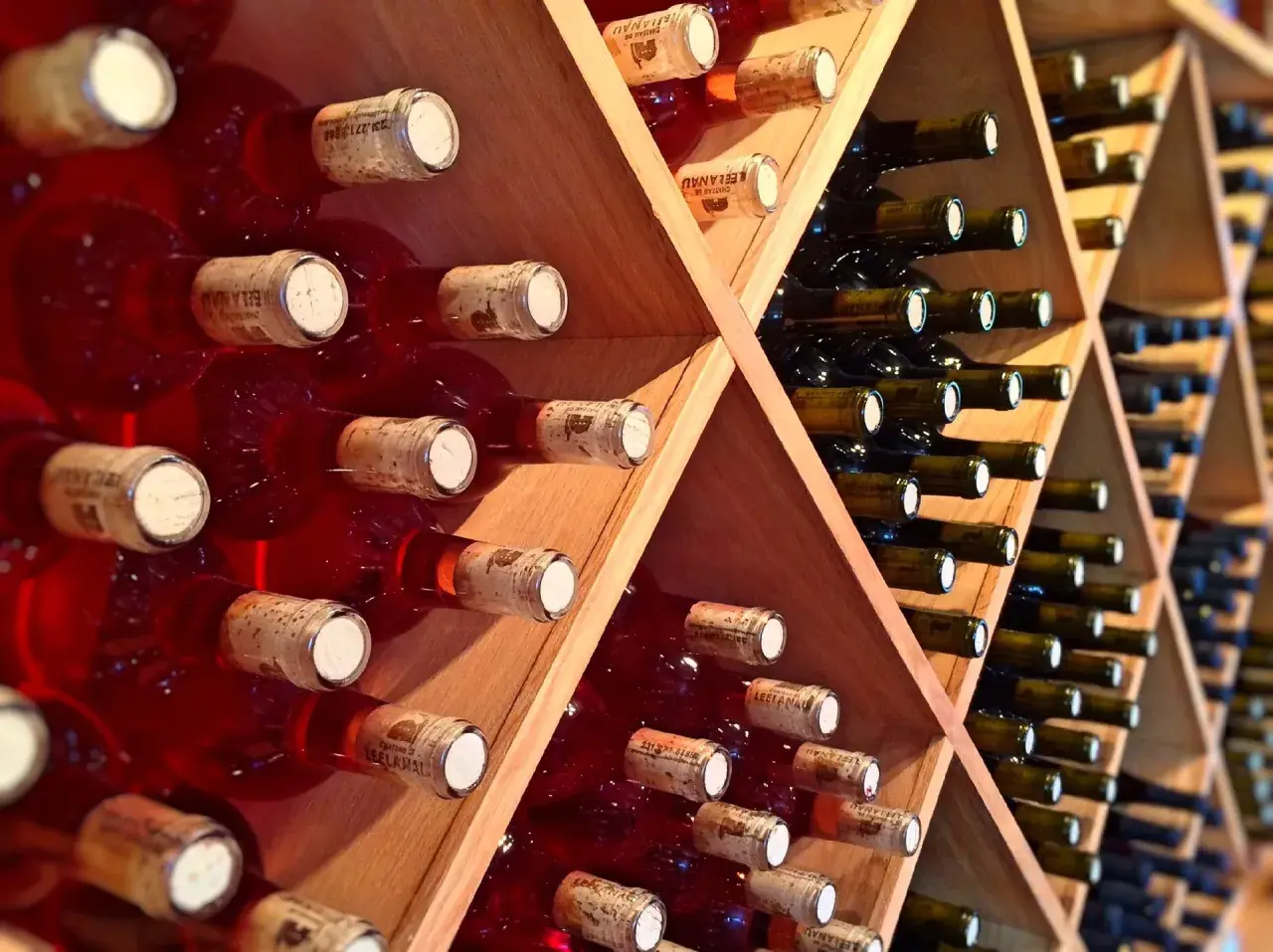 Scaffali di legno pieni di bottiglie di vino rosso, alcune con etichette visibili. Una piccola fioretta di vino attende di essere gustata.