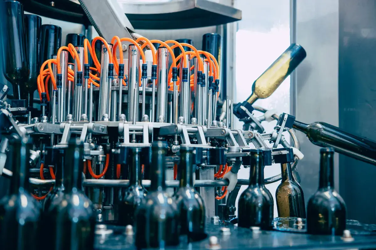 Macchine per la produzione vino: bottiglie in vetro in lavorazione su un nastro trasportatore, con tubi arancioni e componenti metallici.