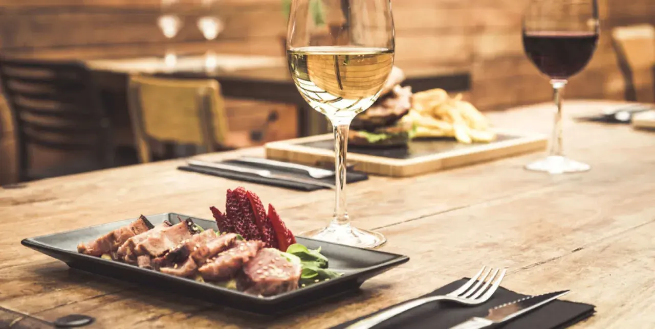 Un bicchiere di vino bianco, perfetto vino bianco per carne alla brace, accanto a un piatto di carne affettata e fragole su un tavolo di legno.