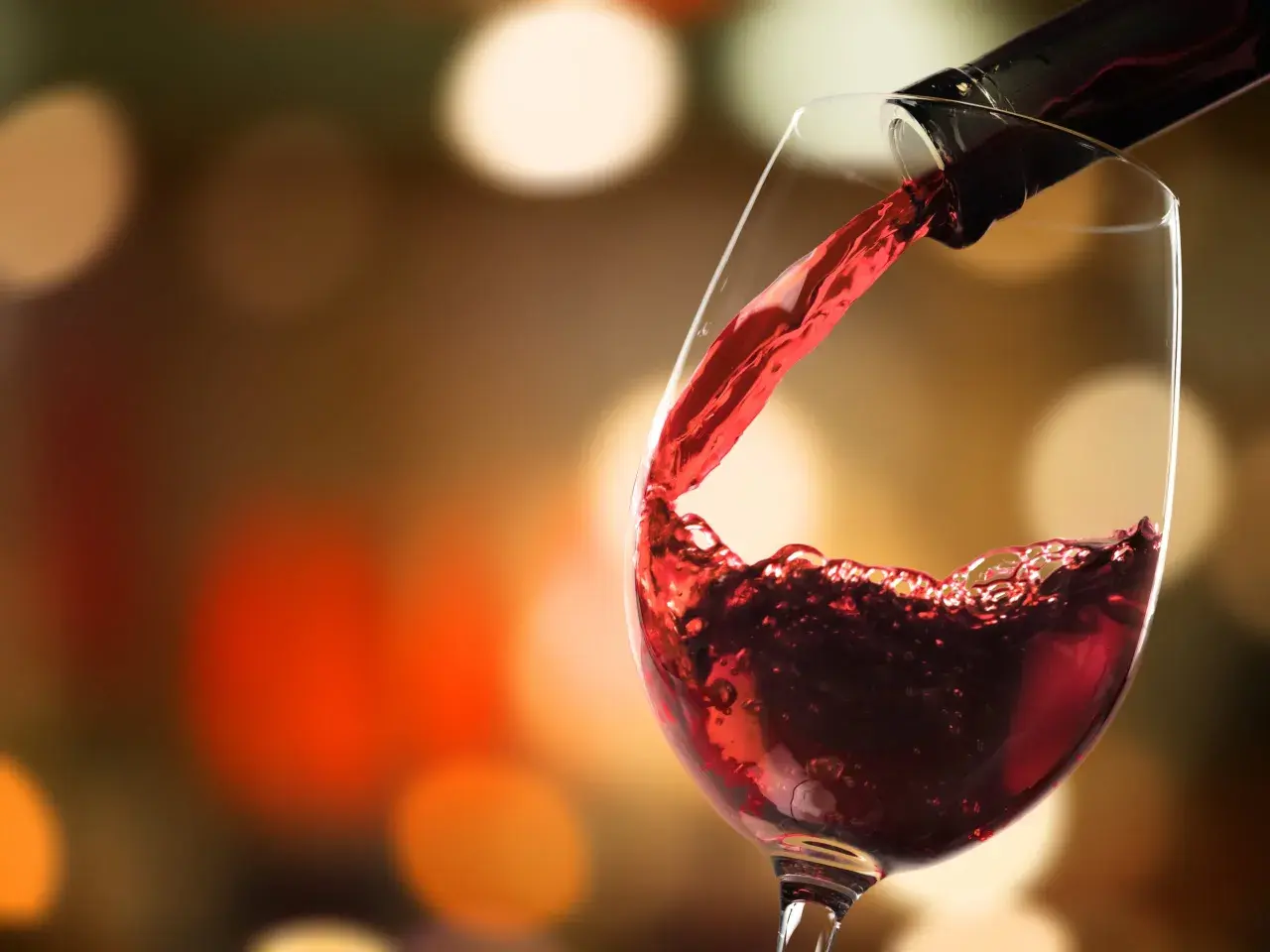 Versare vino rosso in un bicchiere, un momento allappante significato di piacere e convivialità, con luci sfocate sullo sfondo.