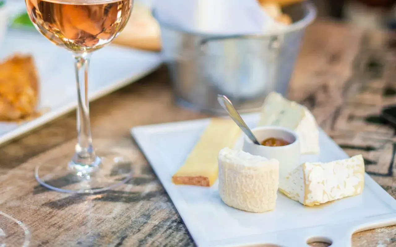 Calice di vino rosato accanto a un tagliere di formaggi, con un assaggio di passito di Pantelleria.