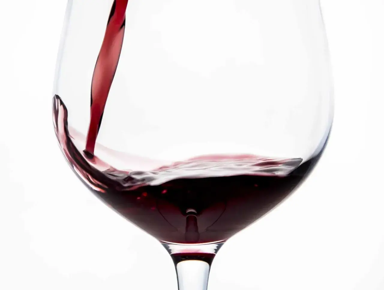 Vino rosso porpora versato in un calice, creando un vortice invitante.