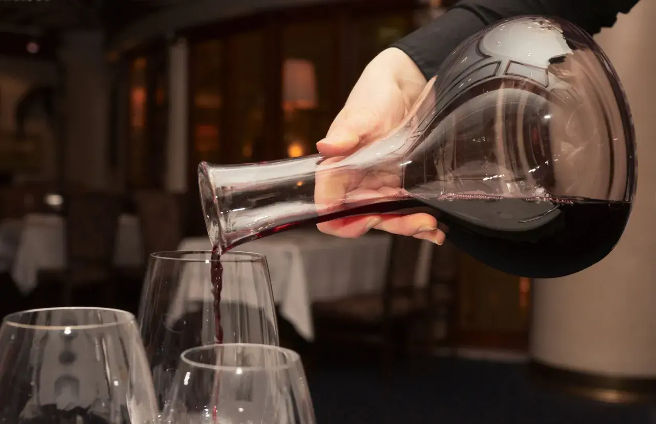 Mano versa vino rosso da una caraffa in bicchieri trasparenti, creando un'atmosfera elegante.