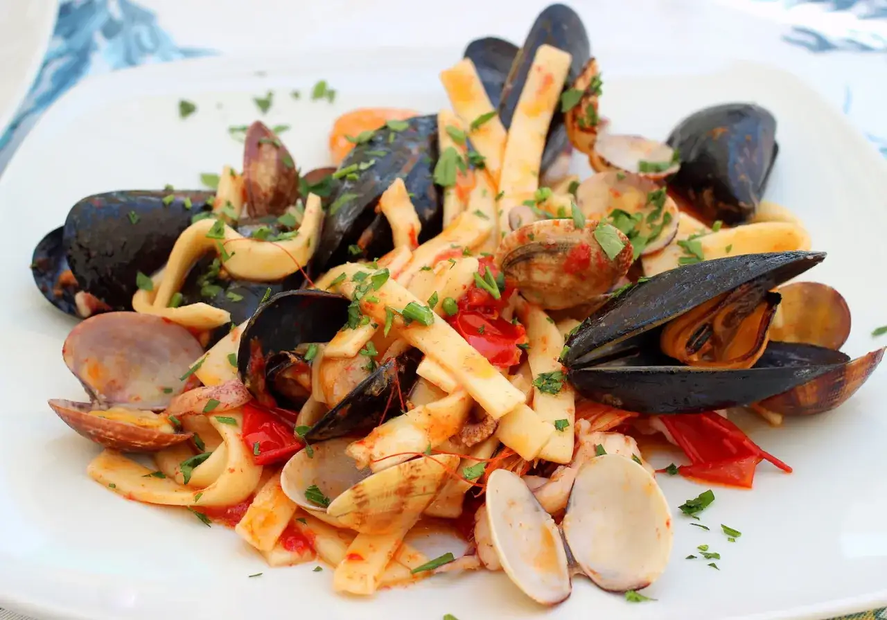 Un piatto di pasta con frutti di mare: cozze, vongole, calamari e gamberi, condito con pomodoro e prezzemolo. Un delizioso pesce bianco in un piatto ricco di sapori marini.