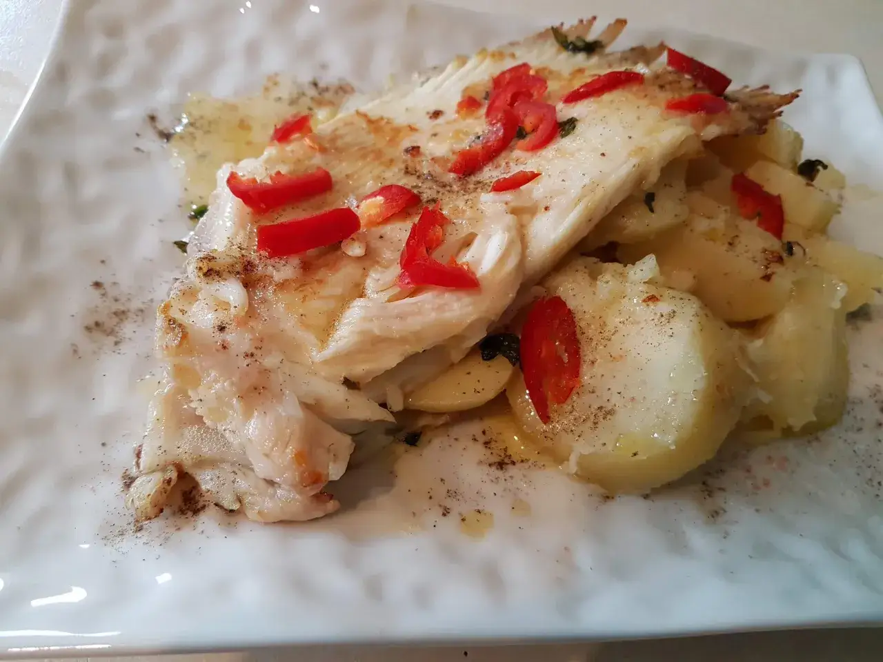 Delizioso pesce razza cotto al forno con patate, peperoncino rosso e erbe aromatiche.