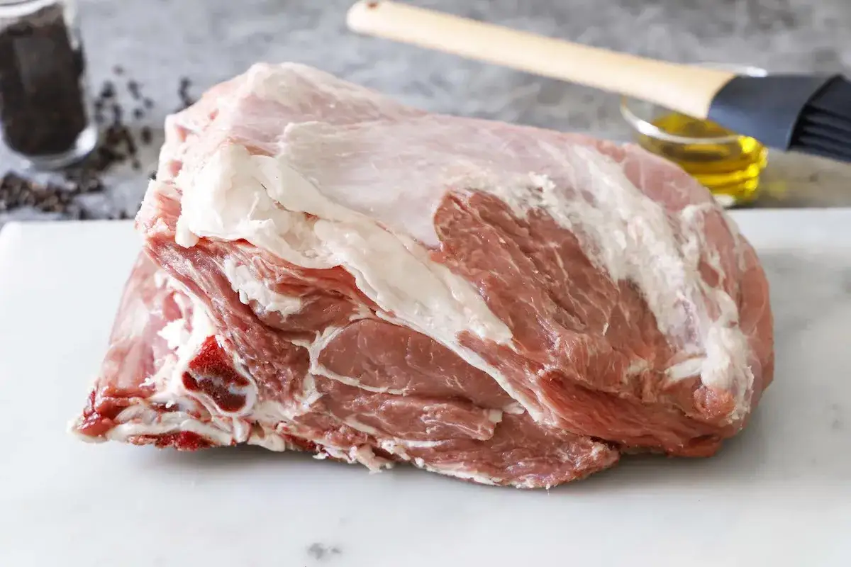 Un succulento petto di vitella crudo, pronto per essere cucinato. Sullo sfondo, pepe nero, olio e un pennello da cucina.