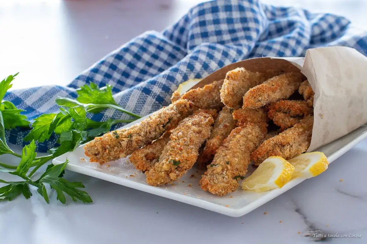 Un sacchetto di carta marrone trabocca di croccanti alici fritte, guarnite con prezzemolo fresco e spicchi di limone.