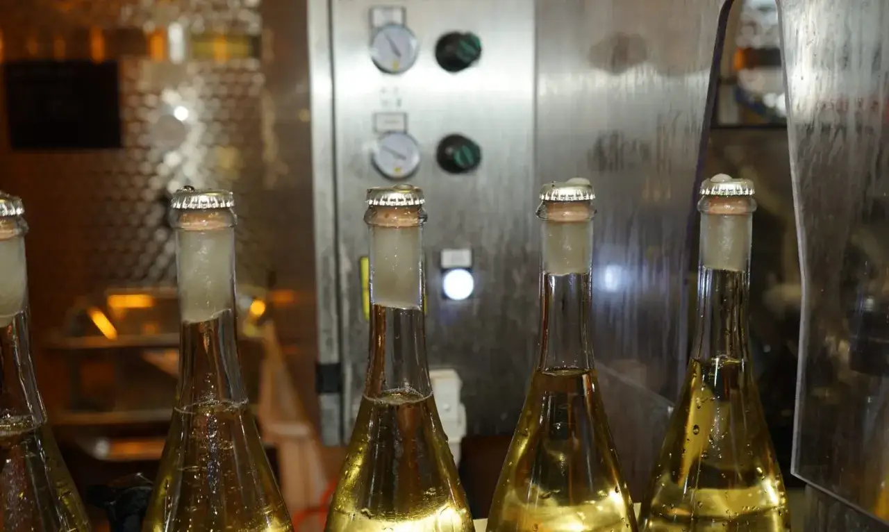 Bottiglie di vino pronte per la sboccatura, con tappi a corona e macchinari industriali sullo sfondo.