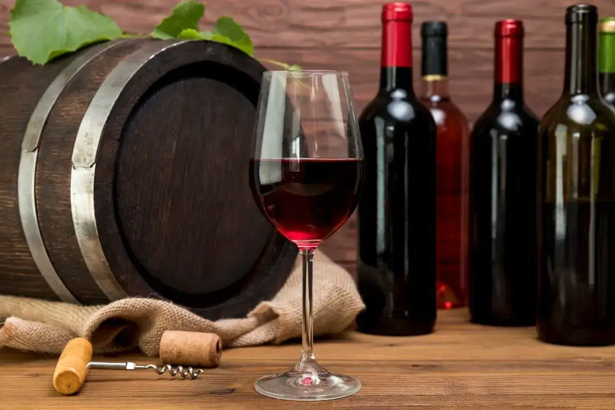 Botte di legno, bicchiere di vino rosso e bottiglie: un'ambientazione perfetta per scoprire come conservare il vino rosso.