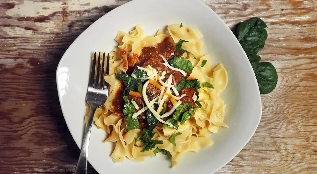 Un piatto di pasta fresca con sugo, spinaci e formaggio, pronto per essere gustato con un buon vino.