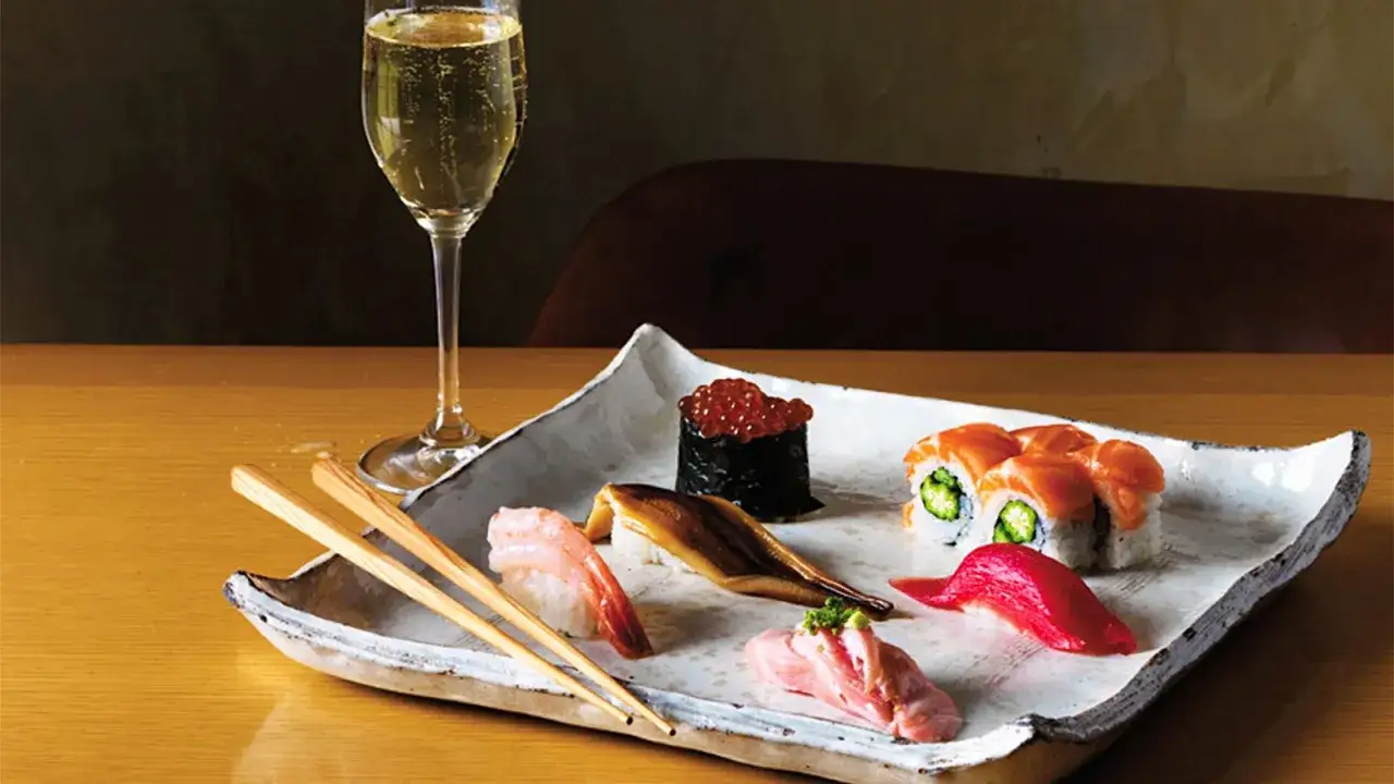 Un bicchiere di vino per sushi, accompagnato da un assortimento di nigiri e maki su un piatto bianco.