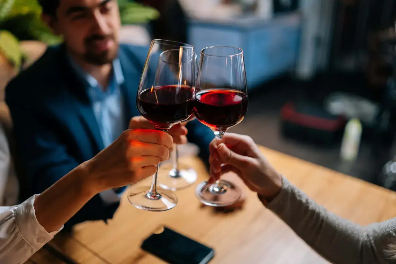 Brindisi con calici di vino rosso durante una degustazione. Un uomo sorride mentre le mani sollevano i bicchieri.