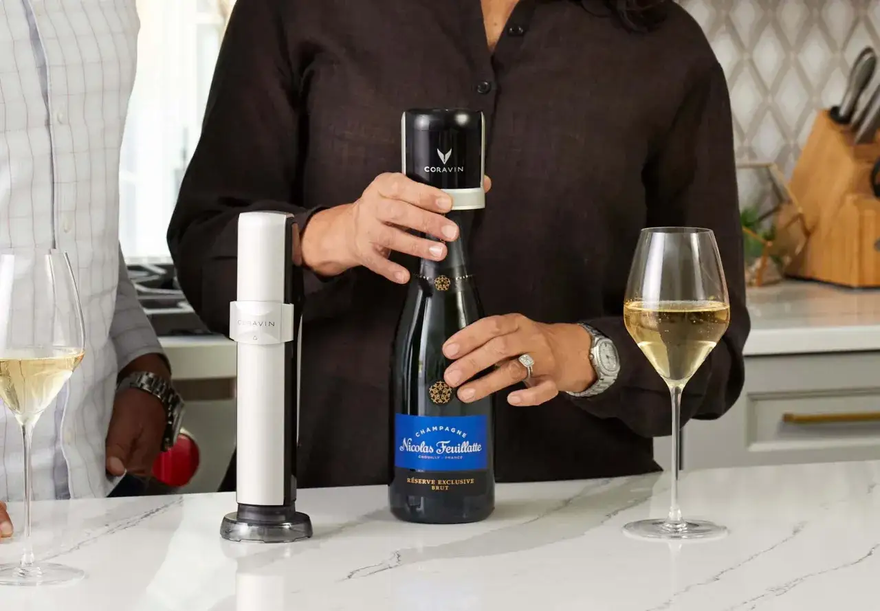 Una persona usa un dispositivo Coravin su una bottiglia di vino con tappo a vite. Due bicchieri di vino sono visibili.
