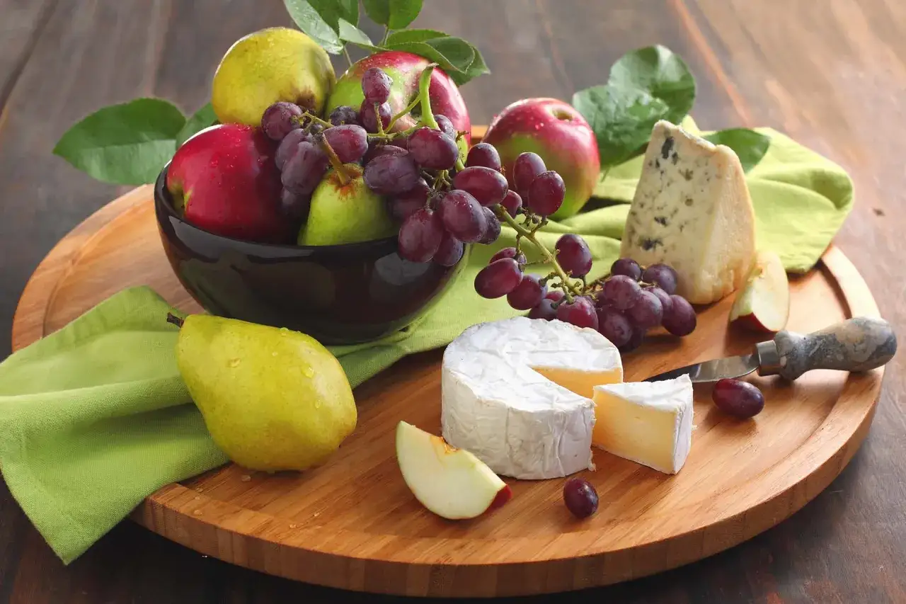 Un perfetto abbinamento uva e formaggio: brie cremoso, gorgonzola piccante, mele rosse, pere verdi e uva rossa su tagliere di legno.