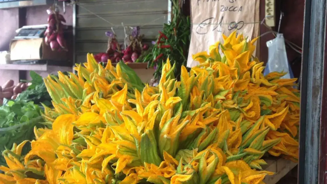 Un mucchio di vivaci fiori di zucca gialli e verdi, pronti per essere cucinati, in un mercato.