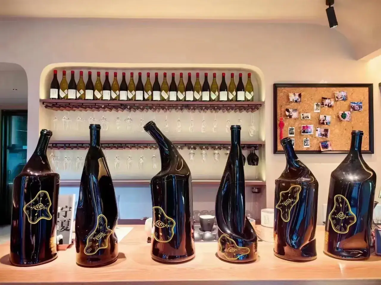 Sei bottiglie jeroboam scure, alcune con forme artistiche e decorazioni dorate, su un bancone di legno.