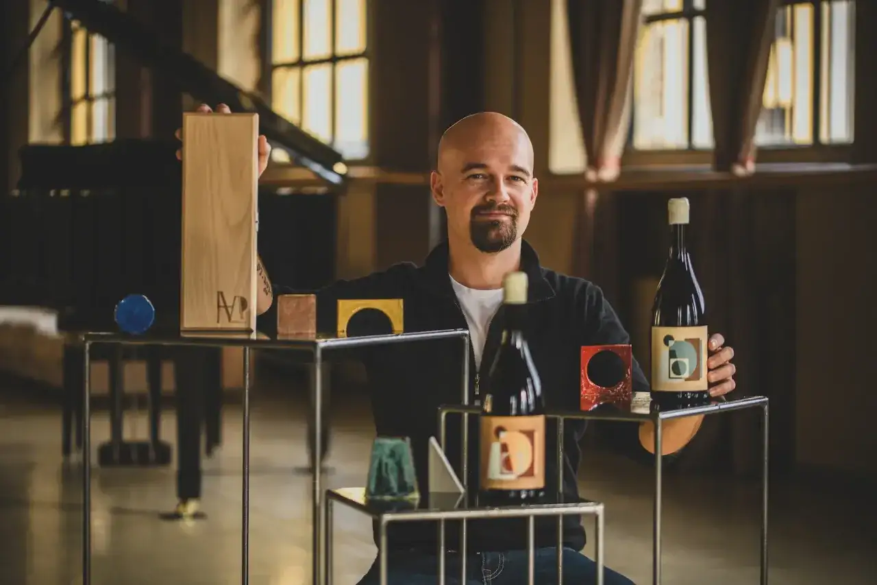 Uomo con barba presenta un blend vino, con bottiglie e scatola di legno.