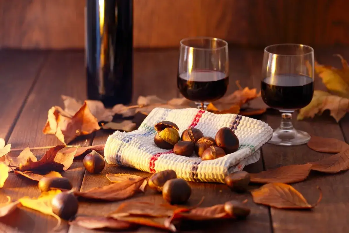 Un bicchiere di vino rosso, perfetto vino per castagne, su un tavolo di legno con foglie autunnali e una bottiglia.