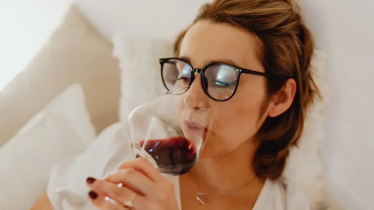 Donna con occhiali beve vino rosso, un momento di relax che ha un allappante significato di piacere e introspezione.
